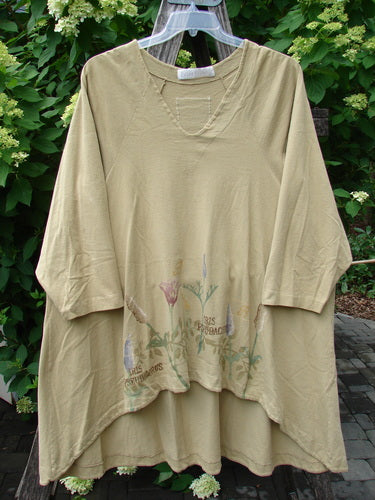 1998 Botanicals Bell Flower Top Iris Pseudacorus Seed Size 2 features a loose, beige tunic with an asymmetrical hem, three-quarter sleeves, and a muted floral print, hanging outdoors against green foliage.