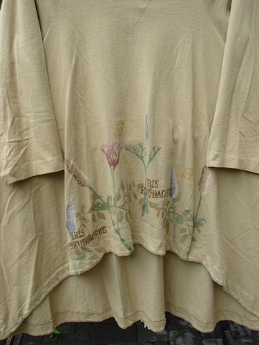 1998 Botanicals Bell Flower Top Iris Pseudacorus Seed Size 2 hangs on a white hanger, featuring a tan cotton tunic with faded iris botanical prints near the hem, showcasing a unique upward scooped hem and belled shape.