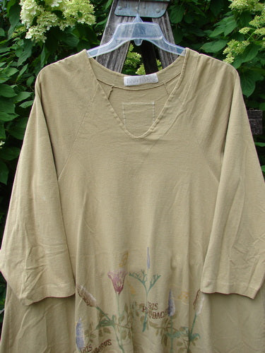 1998 Botanicals Bell Flower Top Iris Pseudacorus Seed Size 2, featuring a loose fit with elbow-length sleeves, faded floral motif along the hem, and a unique upward scooped front hem, hanging outdoors.