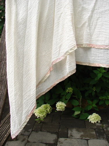 1998 Gauze Over Dress Silk Ribbon Unpainted Chalk Size 2, draped outdoors, showcases lightweight cotton gauze fabric with pink trim, swaying gently above stone ground and hydrangeas, embodying Bluefishfinder.com's vintage elegance.
