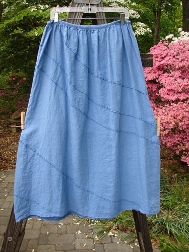 Barclay Linen Diagonal Skirt Unpainted Skylark Size 2 hanging on a clothes rack, showcasing its unique diagonal stitchery and slightly widening shape.