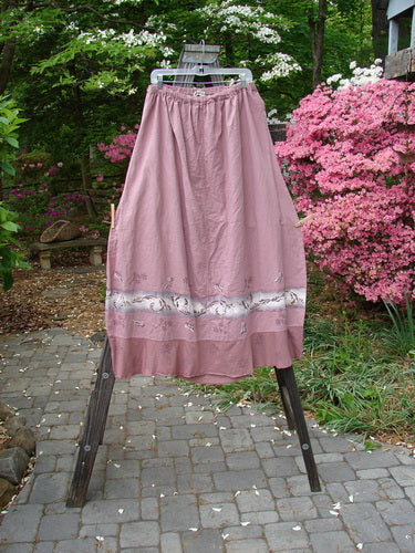 Barclay Linen Duet Skirt Falling Fern Dried Rose Size 2 displayed on a rack, showcasing its unique bell shape, sectional panels, and floral-themed paint accents.