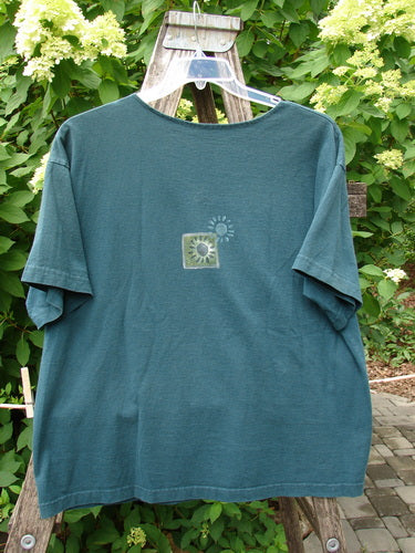 1996 Short Sleeved Promo Tee Old Frenchtown Field Viridian Size 1 displayed on a hanger, showcasing its drop shoulders, square boxy shape, and central square graphic against a natural outdoor setting.