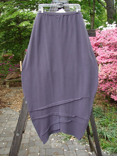 2000 NWT Thermal Awen Skirt Larger Elastic Unpainted Eggplant Size 2 displayed on a wooden stand, showcasing its full elastic waistband, generous lower bell shape, and textured flattened diagonal hemline.