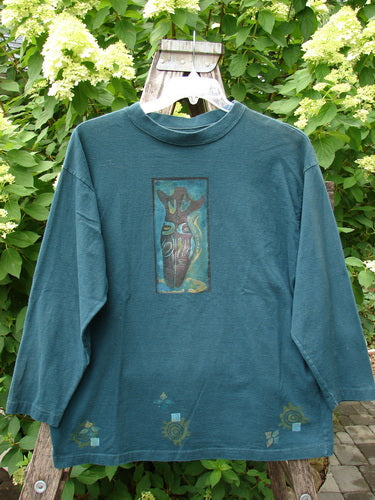 1996 Long Sleeved Tee Primitive Mask Viridian Size 1, displayed on a hanger, features abstract heart-style front print, geometric motifs on hem, and cozy long sleeves, embodying Blue Fish's vintage, expressive style.