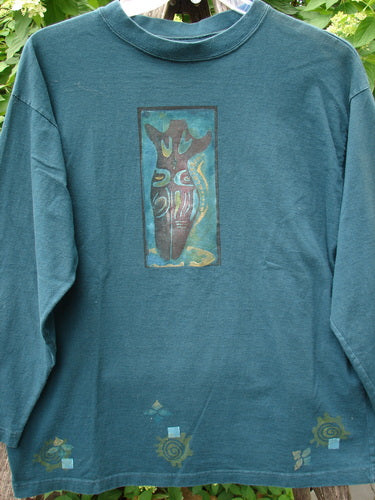 1996 Long Sleeved Tee Primitive Mask Viridian Size 1, featuring a teal hue and abstract earthy print with swirling ochre details, hanging outdoors. Decorated hem motifs echo the vintage Blue Fish creativity.