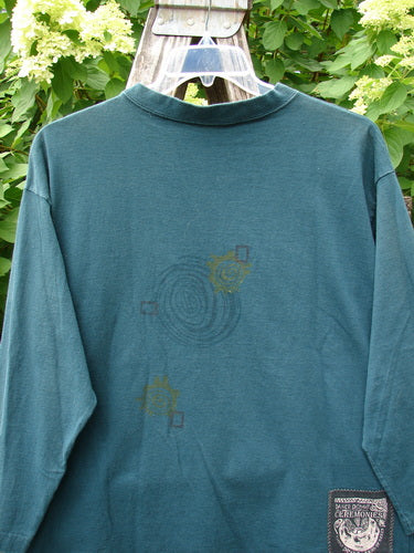 1996 Long Sleeved Tee Primitive Mask Viridian Size 1, showcasing faint graphics and a signature Blue Fish patch, hangs on a wooden ladder, embodying Bluefishfinder.com's vintage charm and individuality.