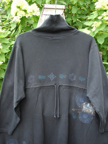 Barclay Interlock Turtleneck Pullover Tunic Top Celtic Night Black Size 2 hangs on a wooden hanger, showcasing its high collar, three-quarter sleeves, drawstring waist, and subtle blue stencil prints.