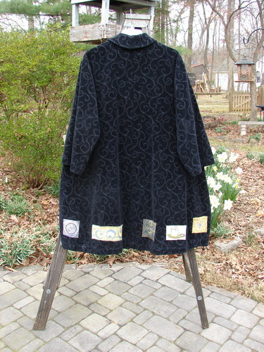 1999 Patched Poet's Coat Holiday Time Black Size 0 on a rack, featuring a vine-patterned pile, oversized floppy pockets, and colorful patched hem, displayed against an outdoor backdrop.