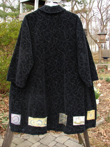 1999 Patched Poet's Coat Holiday Time Black Size 0, featuring a swirl design, oversized button closures, diagonal front pockets, and a varying hemline, displayed on a clothes rack.