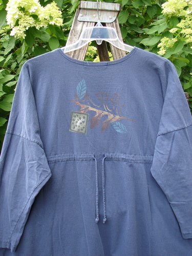 1996 Long Sleeved Pop Top Fall Leaves Niagara OSFA, a blue tunic dress with botanical graphic and drawstring waist, hangs on a trellis. Features include a rounded hemline, drop shoulders, and oversized front pocket.