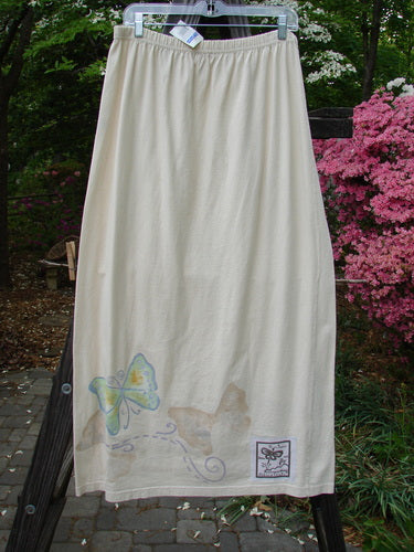 1999 NWT Straight Skirt Butterfly Natural Size 2, featuring a butterfly design around the hem, displayed on a clothesline with pink flowers nearby. Made from organic cotton with a full elastic waistband.