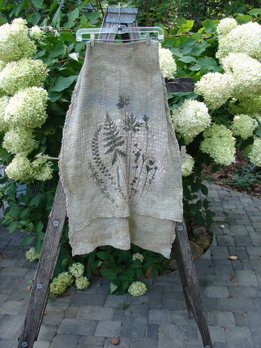 Barclay Crinkle Cotton Scarf Morning Fern Mottled Wheat OSFA, draped over a wooden ladder, features fern and grass prints, showcasing its soft texture and slight stretch, perfect as a summer accent.