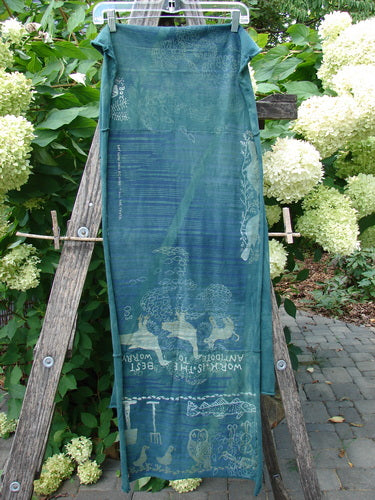 Barclay Wide Sectional Scarf Wrap Forest Animals Mottled Green OSFA draped on a wooden ladder, showcasing whimsical motifs and quotes, ideal for versatile styling as a shawl or scarf.