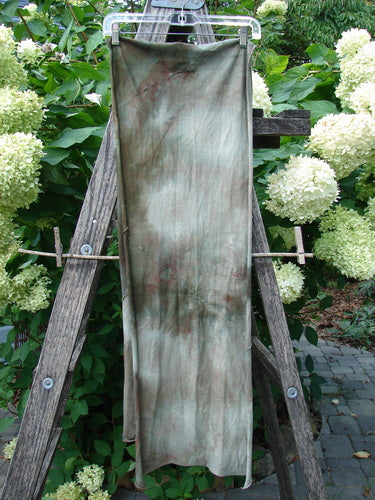 Barclay Diagonal Sectional Scarf Wrap in Unpainted Mottled Night Storm draped on a hanger, showcasing its sweet finished curly edges and exterior diagonal seams against lush foliage, embodying vintage Blue Fish creativity.