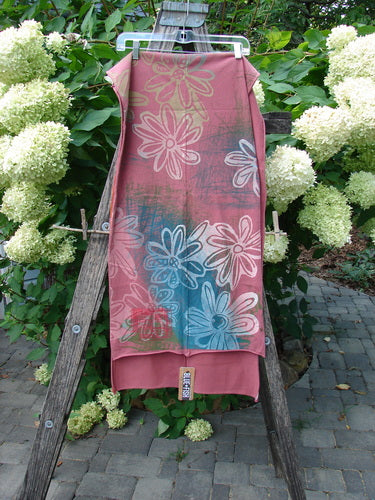Barclay NWT Wide Sectional Scarf Daisy Desert Rose OSFA draped over a wooden ladder in a garden, showcasing its daisy pattern and sweet unfinished rolled edges, against lush greenery and hydrangeas.