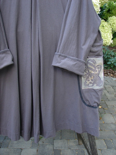 1998 Tiddly Winks Jacket Butterfly Madeira Size 2: A knee-length, loose-fitting coat with three-quarter sleeves, decorative skull motif, deep pockets, and replaced decorative buttons, hanging outdoors against a stone patio backdrop.