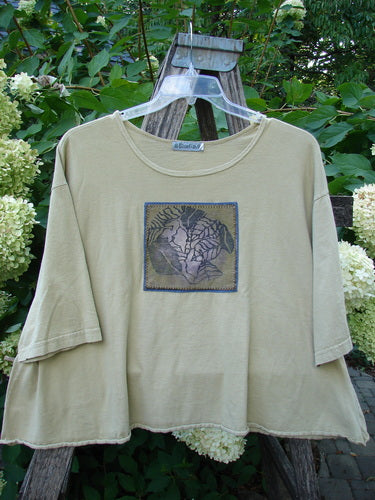 Barclay PMU Patched Short Sleeved Crop A Lined Tee Honey Size 2, featuring a stylized tree motif patch, hangs on a trellis, showcasing its organic cotton fabric and unique upcycled design.