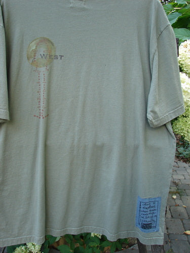 2000 Short Sleeved Tee Celtic Exploration Park Size 2 features a muted olive tone, circular globe motif on the chest, and a blue rectangular patch near the hem, embodying Bluefishfinder.com's vintage, creative style.