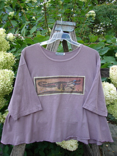 Barclay PMU Patched Short Sleeved Crop A Line Tee Dark Mallow Size 2, featuring elbow-length sleeves and a raw-edge hem, hangs on a ladder, showcasing a stylized crocodile motif patch.