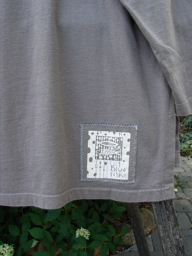 1999 Long Sleeved Vented Tee Orchid Sprig Shale Size 1 draped outdoors; features ribbed neckline, vented sides, and signature Blue Fish patch with fish illustration, embodying Bluefishfinder.com’s vintage creative expression.