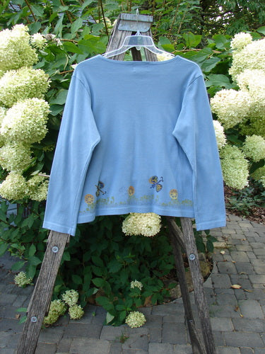 1999 Round Neck Rib Top Butterfly Blue Stone Size 2 on a clear hanger, showcasing a slightly cropped, boxy shape with a seashell-themed hem, against a lush garden backdrop. Perfect vintage Blue Fish piece.