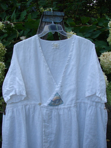 1999 Linen Adjustable Wrap Dress Fish White OSFA: A loose-fitting dress with a deep V-neck, elbow-length sleeves, empire waist, and flowing skirt, featuring pearl buttons and fish print wrap, set against greenery.