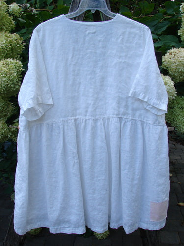 1999 Linen Adjustable Wrap Dress Fish White OSFA, featuring a loose fit with short sleeves, a gathered waist, and a full skirt, displayed on a hanger against leafy shrubs.