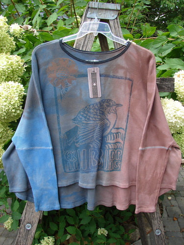 Barclay NWT Thermal Crop Top Finch Mottled Bibbi Blue OSFA displayed on a wooden trellis, features a tie-dye pattern with bird and flower graphics, showcasing its drop shoulders and unique hem design.