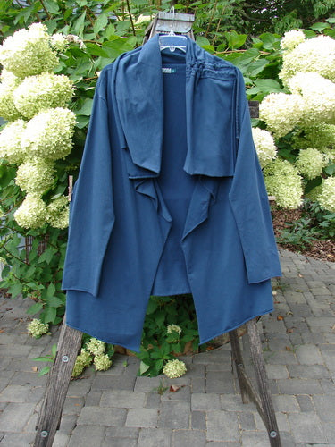 Barclay Cotton Lycra Gather Collar Open Front Jacket Unpainted Navy Size 2 drapes elegantly on a wooden ladder, showcasing its waterfall-style collar and long sleeves against lush hydrangeas.