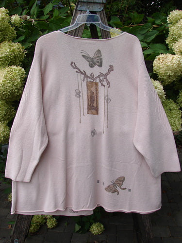 The 1994 2 Button Cardigan Sweater Magical Garden Pink Granite OSFA features a dusty-pink knit, elbow-length sleeves, and butterfly motifs, elegantly draped over a rustic ladder.