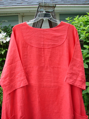 Barclay Linen Cross Over Dress Golden Lookout Geranium Size 2 displayed on a hanger, showcasing its V-neckline, drop shoulders, and varying side lengths.