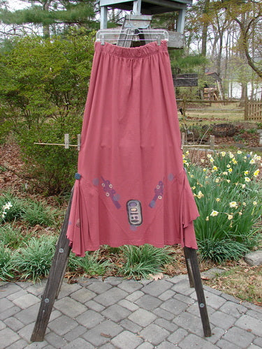 1996 Dubuffet Skirt Abstract Ember Size 2: Organic cotton skirt on a wooden stand, featuring a full elastic waistband, side panels with pleats and buttons, and removable painted flutters with lettuce edging.