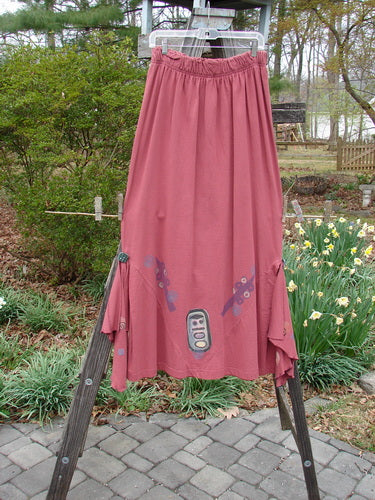 1996 Dubuffet Skirt Abstract Ember Size 2, featuring a full elastic waistband, pleated diamond-shaped side panels with painted buttons, and removable half-circle flutters, hanging on a clothesline.