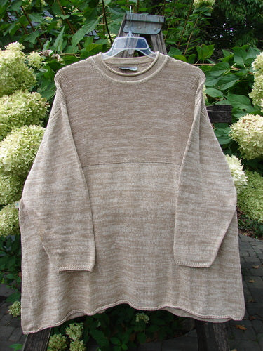 Jennifer's Rollneck Sweater Marled Aspen, OSFA, draped on a clear hanger outdoors. The knit's textured design and generous A-line shape are showcased against a backdrop of lush foliage and hydrangeas.