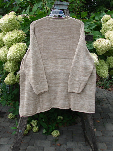 Jennifer's Rollneck Sweater Marled Aspen OSFA on a hanger over a wooden ladder, set in front of white hydrangeas, showcasing its generous shape and textured knit in a garden setting.