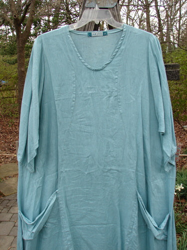 Barclay Linen Side Pocket Tab Tunic Dress Unpainted Mint Size 2 displayed on a clothes rack, showcasing its oval neckline, curved vertical seams, and two drop pockets.