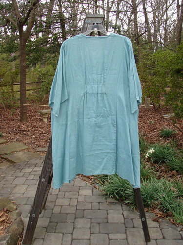 Barclay Linen Side Pocket Tab Tunic Dress Unpainted Mint Size 2 displayed on a wooden stand, showcasing its scooped neckline, curved seams, wide short sleeves, and drop pockets.