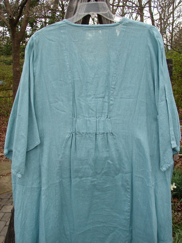 Barclay Linen Side Pocket Tab Tunic Dress Unpainted Mint Size 2 displayed on an outdoor swing, showcasing its oval neckline, drop flop pockets, and short wide sleeves.