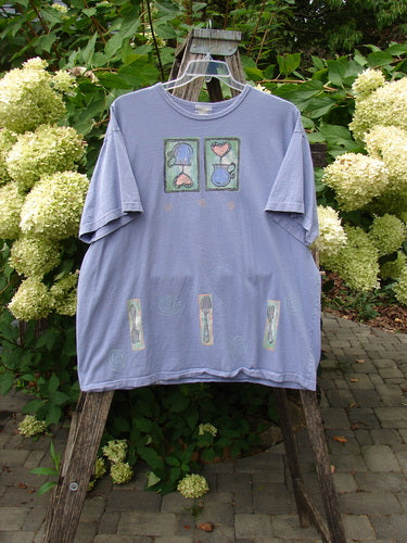 1999 Short Sleeved Tee Reverse Heart Vase Iris Size 2 displayed on a wooden ladder. Features block-print artwork with heart and vase motifs, rolled neckline, and signature Blue Fish patch, highlighting vintage Blue Fish style.