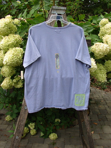 1999 Short Sleeved Tee Reverse Heart Vase Iris Size 2, displayed on a wooden ladder in a garden, features a weathered look with painted details and Blue Fish patch, embodying vintage charm.