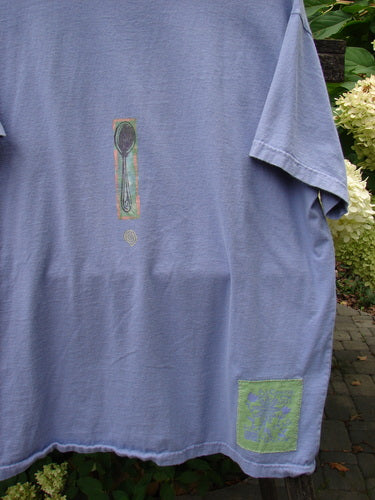 1999 Short Sleeved Tee Reverse Heart Vase Iris Size 2 draped over foliage, featuring a vertical spoon silhouette on the chest and a blue floral patch near the hem, crafted from organic cotton.