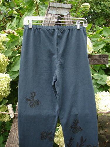Barclay NWT Cotton Lycra Straight Pant Botanicals Lux Silhouette Size 1, featuring a butterfly print, hangs on a garden chair, highlighting its forgiving fit and vintage design appeal from BlueFishFinder.com.