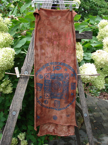 Barclay Diagonal Scarf Wrap Belief Spirit Magic Mottled Rust OSFA draped on a weathered ladder, displaying deep blue circular designs with symbols, set against lush garden foliage and hydrangeas.