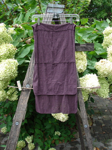 Barclay Gauze Sectional Scarf Wrap in Deep Burgundy hangs on a clear hanger over a weathered ladder, showcasing its sweet finished edges and exterior horizontal sectional seams against a lush green backdrop.