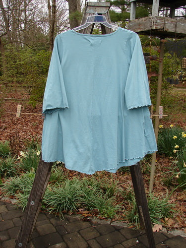 Barclay Three Quarter Sleeved Cafe Pocket Top Long Stem Dusty Aqua Size 1 displayed on a wooden rack, showcasing its A-lined tunic shape, three-quarter sleeves, and double side entry kangaroo pocket.