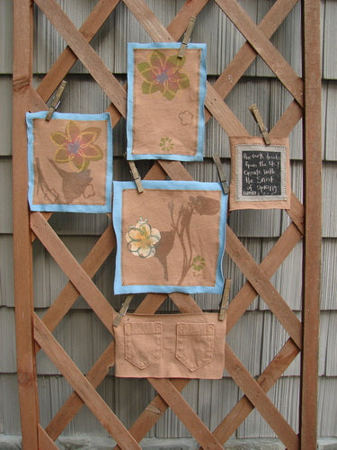 Image alt text: The PMU 2000 Spring Floral Pocket Patch Set - a group of fabric pieces on a wooden lattice, featuring a close-up of a towel, a close-up of a bag, a black square with white text on it, and a cloth with a flower on it.