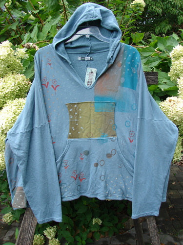 Barclay NWT Fleece Modal Hip To Be Square Hoodie Rain Flower Sea OSFA on a bench, featuring a kangaroo pocket, chartreuse and aqua chest patch, and scattered floral motifs, perfect for creative expression.