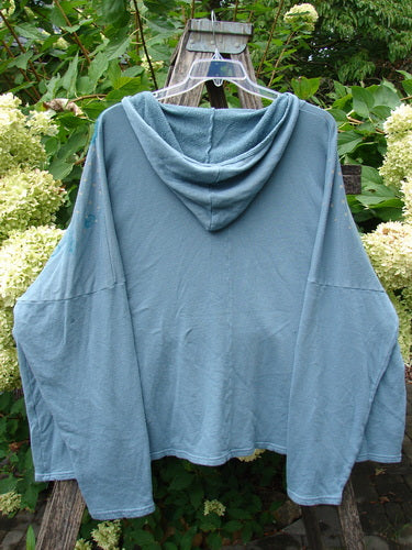 Barclay NWT Fleece Modal Hip To Be Square Hoodie Rain Flower Sea OSFA displayed on a clear hanger, draped over a wooden trellis with leafy hydrangeas in a garden setting.