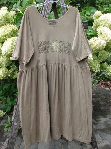 1994 Flower Garden Dress Wind Medallion Bark Size 2: Olive-green knee-length dress with scoop neckline, elbow-length sleeves, gathered skirt, circular chest print, and removable pocket, hanging outdoors suggesting a whimsical garden party style.
